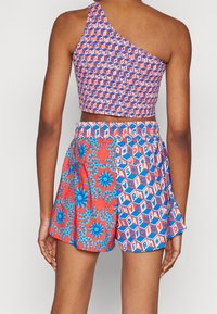En axelbar crop top med geometrisk tryck, kombinerat med röda shorts som har blå blommönster och spiralmönster. Elastisk midja, färgglad och livfull.