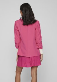 Rosa blazer med rynkade ärmar och feminin passform, parat med en matchande lager-på-lager rosa kjol. Slätt tyg, enkel design och inga synliga mönster.