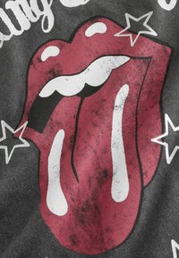 Lèvres rouges avec un graphique de langue étendue sur tissu noir, avec des reflets blancs et des étoiles autour de la bouche.