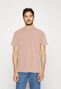 T-shirt rosa chiaro a maniche corte in tessuto morbido, con un classico collo a giro e un piccolo logo sul lato sinistro del petto.