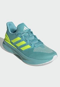 Zapatilla deportiva en color azul verdoso con acentos en verde lima, parte superior de malla, superficie texturizada, diseño de tres rayas, punta redondeada y suela blanca.