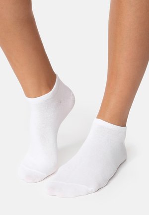 Two feet wearing plain white ankle socks on a white surface, one foot slightly raised on toes.