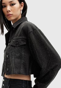 Beskyttet svart denimjakke med klassisk krage, frontlommer og teksturerte, utsmykkede ermer med skinnende detaljer.
