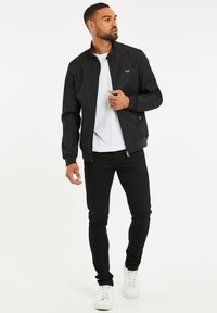 Svart bomberjacka med ståkrage, framdragkedja och ribbade ärmslut. Bärs över en vit t-shirt och ihop med svarta jeans och vita sneakers.