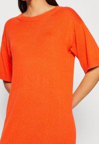 Krátký rukáv oranžový svetr vyrobený z měkkého pleteného materiálu, s kulatým výstřihem a volnějším střihem, s hladkou texturou.