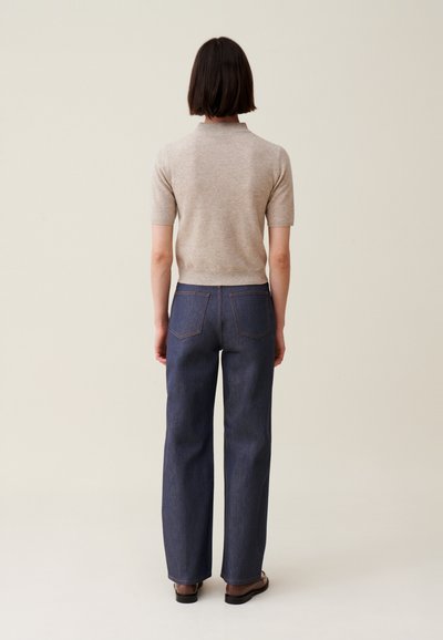 Top di maglia beige a maniche corte abbinato a jeans in denim a gamba larga blu scuro. I jeans presentano due tasche posteriori e un design a taglio dritto.