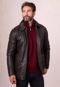 Brown leather jacket with a collared neck and zip front, paired with a burgundy sweater and dark jeans. Smooth texture and fitted design.