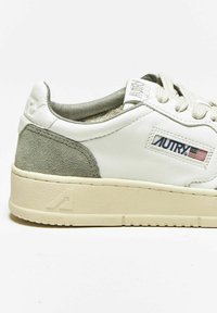 Sneakers bianchi in pelle con dettagli in suede grigio, lacci piatti e suola beige texturizzata. Presenta etichetta e logo sul tallone.