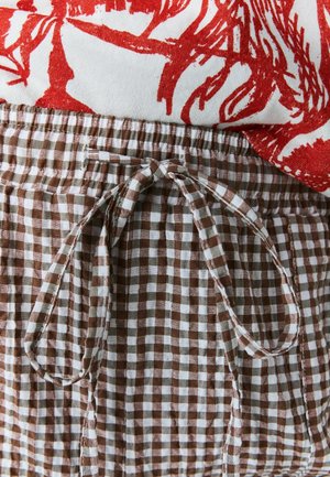 Brown and white checked fabric shorts with an elastic waist and a tied drawstring. A red floral print top partially visible above.