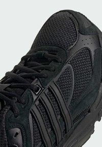 Black athletic shoe featuring a mesh upper, suede accents, and layered rubber sole. Includes black laces and textured detailing.