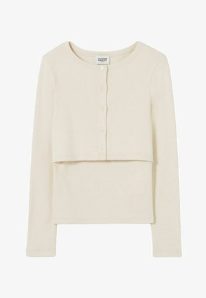 Cardigan cropped a maniche lunghe e bottoni di colore crema indossato sopra un top senza maniche abbinato di colore crema.