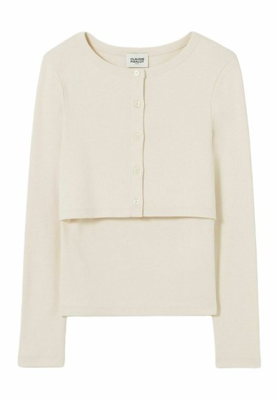 Gilet cropped à manches longues crème avec boutons, superposé à un haut sans manches crème assorti.