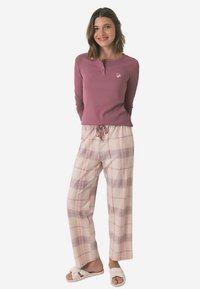 Pitkähihaisen, resuilevan violetin paidan napillinen nappilista; ruudulliset, väljäntuntuiset vaaleanpunaiset housut, joissa on violetteja ja sinisiä yksityiskohtia; valkoiset sandaalit.