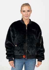 Giacca bomber in faux fur nera con zip frontale, polsini e vita a coste. Tasche laterali e un piccolo logo accentato sul petto.