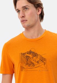 Oranje t-shirt met korte mouwen van zachte stof, met een zwarte lijntekening van bergen en de zon. Logo afgedrukt in de rechteronderhoek.