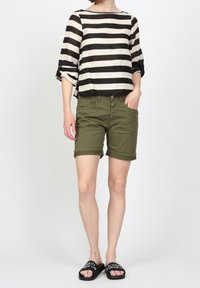 Svart och vitrandig linneblus med vida ärmar, kombinerad med olivgröna shorts. Svarta slip-on sandaler har vit textdetalj.