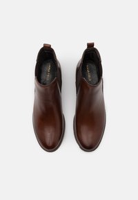 Bottes cheville en cuir marron avec une finition lisse, des panneaux latéraux élastiques et une semelle texturée. Étiquetées "ANNA FIELD" à l'intérieur.