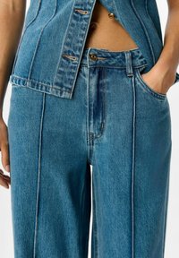 Jeans de mezclilla en azul claro, con un diseño de pierna recta, costuras visibles, un cierre de botón y bolsillos frontales.