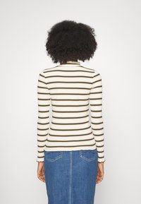 Gestreiftes Langarmoberteil, cremefarbener Grundton mit schmalen schwarzen und senfgelben Streifen. Weicher Stoff, figurbetonter Schnitt und gewellter Saum. Getragen mit einem Jeansrock.
