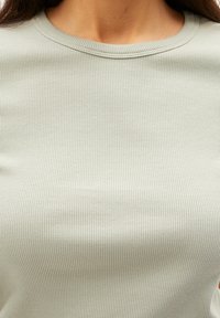 Světlé zelené žebrované tričko s kulatým výstřihem. Látka má vertikální pruhy, které zdůrazňují hladkou texturu a přiléhavý střih.