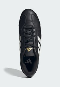 Schwarze Adidas Sneaker mit weißen Streifen, schwarzen Schnürsenkeln und goldenem Logo auf der Zunge, aus einer Vogelperspektive auf einem hellen Hintergrund gezeigt.