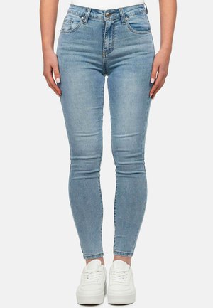Hellblaue Damen Skinny Jeans mit hoher Taille, ausgestattet mit Fronttaschen, Gürtelschlaufen und einer glatten Textur. Kombiniert mit weißen Sneakers.
