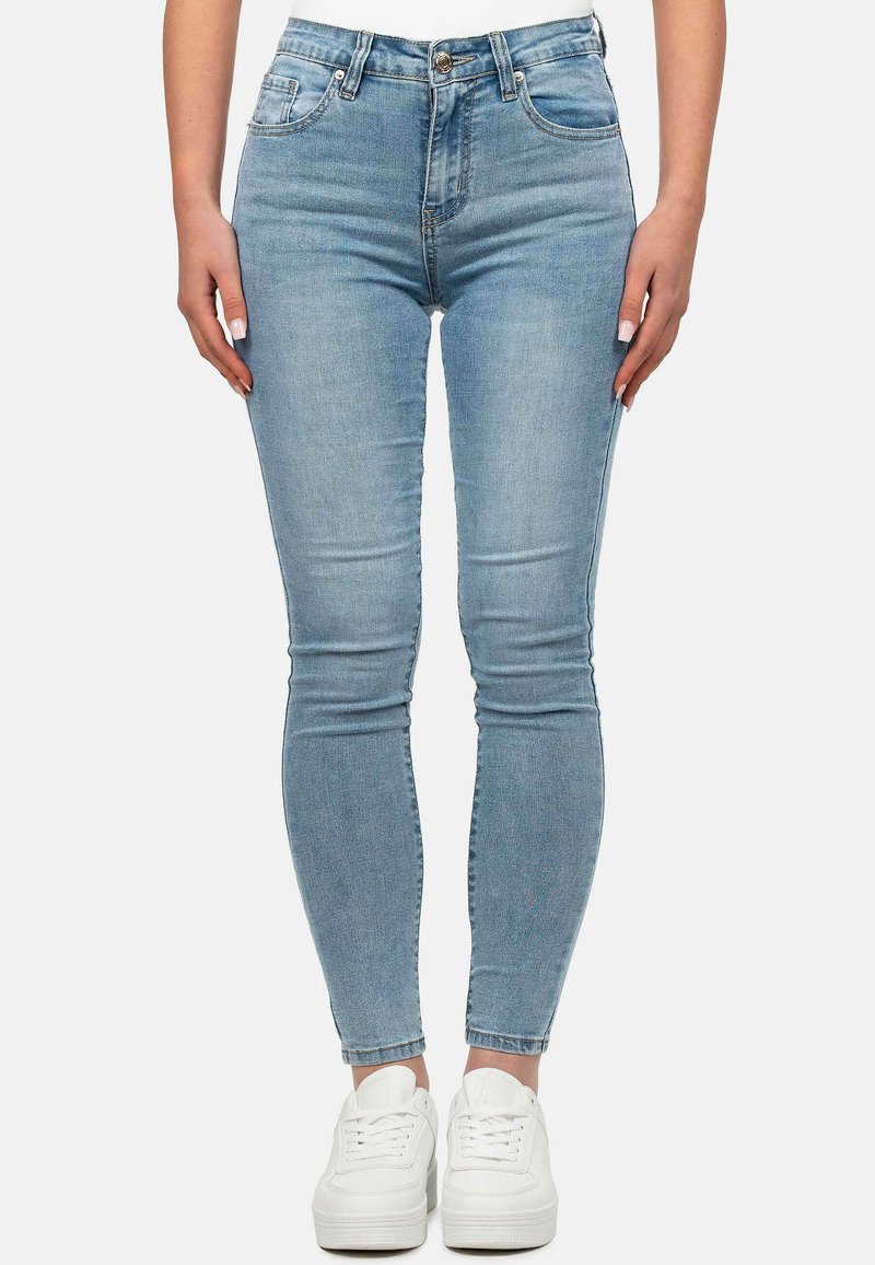 Jean skinny en denim bleu clair avec taille haute, présentant des poches avant, des passants de ceinture et une texture lisse. Associés à des baskets blanches.