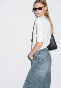 Weißes Langarmhemd, hellblaue weit geschnittene Jeans, schwarze Handtasche und dunkle Sonnenbrille. Minimalistisches Design mit einer weichen Textur.