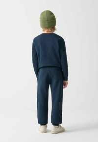 Tamsiai mėlynas medvilninis džemperis ir atitinkamos kelnės, su žalia megzta kepure, kelnių gale esantis kišenės detalė.