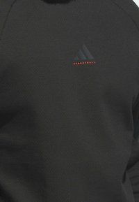 Schwarzer sportlicher Sweatshirt aus strukturiertem Stoff. Mit kleinem schwarzem Adidas-Logo und dem Wort "BASKETBALL" in Rot.