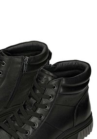 Zwarte leren enkelboots met een textuurafwerking, voorzien van een vetersluiting, een zijrits en een gegroefde rubberen zool. Accentstiksels zichtbaar.
