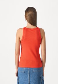 Top de tirantes rojo con textura acanalada, cuello redondo y tirantes anchos, combinado con una falda de mezclilla. Textura suave y diseño ajustado.