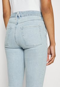 Ljust blå denimjeans med en mjuk elastisk midja, två bakfickor och en tapered passform, som visar en slät yta och minimal tvätt.