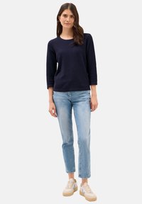 Marineblå stickad tröja med trekvartsärmar, matchad med ljusblå, något slitna jeans och beiga sneakers med blå detaljer.