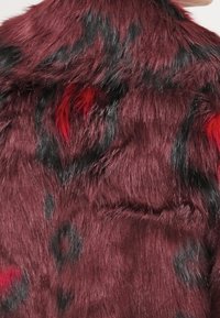 Pelo sintético rojo y negro con una textura suave, que presenta un patrón de manchas oscuras y un tono rico y profundo en toda la superficie.