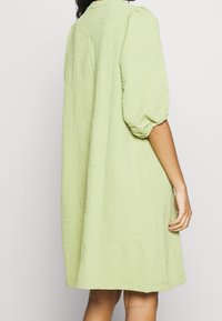 Robe vert pâle en tissu texturé, présentant une coupe ample, des manches bouffantes et un ourlet au niveau du genou. Encolure et design simples.