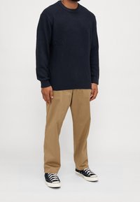 Mörkblå stickad tröja med rund halsringning, kombinerad med ljusbruna byxor och svarta sneakers med vita detaljer och snören.