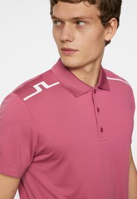Rosa polo skjorta med krage, korta ärmar, placket med tre knappar och vit detalj på axeln. Snyggt, andningsbart tyg.