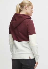 Hettegenser med maroon overdel, kremfarget og grå underdel, myk stoff og en liten merketag i sømmen.