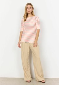 Haut rayé en pêche et blanc avec des manches courtes, associé à un pantalon large beige. Le tissu semble doux et texturé.