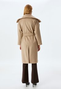 Abrigo de lana beige con un amplio cuello, cintura ceñida con cinturón y mangas largas, que presenta una silueta recta y una abertura en la parte posterior.