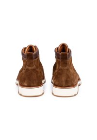 Hnědé suede kotníkové boty s krémovým koženým manžetou a bílou gumovou podrážkou, zdobené švy a poutkem na zadní straně.