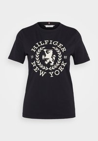 Černé bavlněné tričko s krátkými rukávy, které má bílé vyšívané logo lva v designu vavřínu a text "HILFIGER NEW YORK 1985".