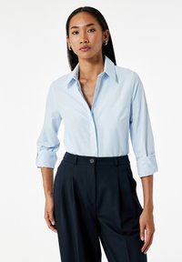 Lichtblauwe overhemdd met opgerolde mouwen en een puntige kraag, gecombineerd met donkere marineblauwe , op maat gemaakte broek, gladde stofstructuur.