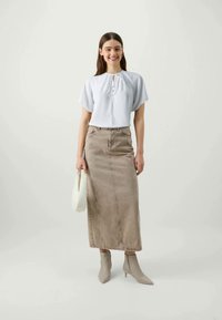 Blusa branca de manga curta com detalhe de laço, combinada com uma saia maxi de ganga bege e botas de tornozelo cinza claro. Design minimalista, texturas suaves.