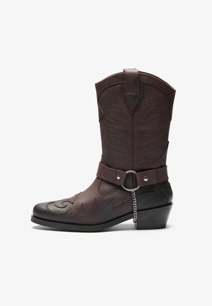 Bottines de cowboy en cuir marron avec des coutures décoratives, un bout pointu et un talon bloc de hauteur moyenne avec une sangle et un détail en chaîne.