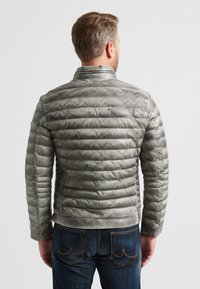 Graue Daunenjacke mit einem gesteppten Design, horizontalen Streifen und Stehkragen. Kombiniert mit dunklen Jeans mit gestickten Akzenten.