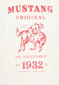 White t-shirt featuring red graphic print of a cowboy riding a horse, with "MUSTANG ORIGINAL" and "INT. JEANS COMPANY" text above.