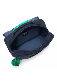 Borsa Kipling blu navy con zip sicura, manico verde e un charm verde peloso attaccato. L'interno è foderato in materiale blu uniforme.