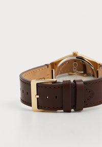 Correa de reloj de cuero marrón con hebilla en tono dorado. Presenta una caja rectangular, textura suave y un detalle de costura visible.